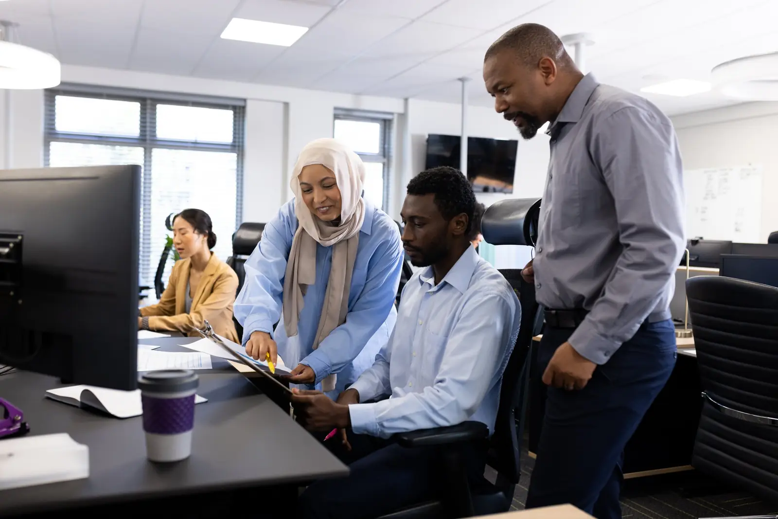A consultant walking two colleagues through a plan at their desk